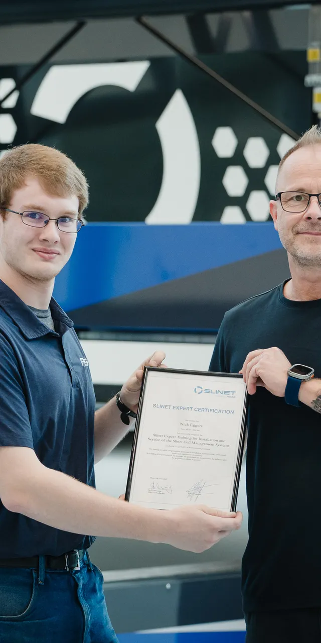 Zwei Mitarbeiter der ASCO Machinery Group mit Zertifikat vor einer Blechbearbeitungsmaschine in der Produktionshalle.