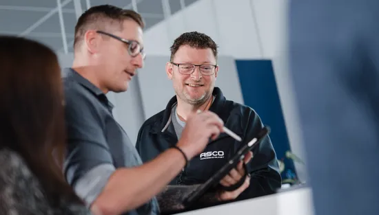Mitarbeiter der ASCO Machinery Group im fachlichen Austausch über ein technisches Bauteil in der Serviceabteilung.