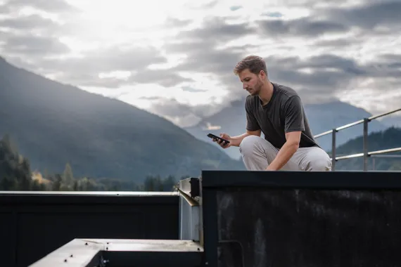 Mitarbeiter nutzt die Variobend V-Mobile App auf einem Smartphone zur mobilen Profilplanung im Außenbereich vor einer Bergkulisse.