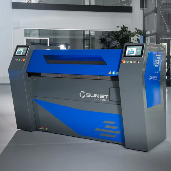 Kompakte Slinet S1.0 Längs- und Querteilanlage mit blau-grauem Maschinengehäuse, platzsparend aufgestellt in einer Produktionshalle.