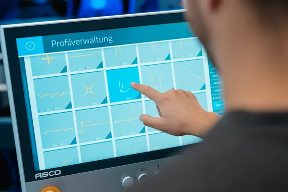 Mitarbeiter bedient die Profildatenbank der Variobend V-Touch Software am Touchscreen mit grafischer Übersicht verschiedener Blechprofile.