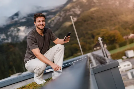 Mitarbeiter nutzt die Variobend V-Mobile App auf einem Smartphone zur mobilen Profilplanung im Außenbereich vor einer Bergkulisse.