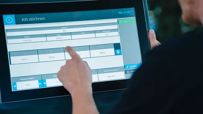 Mitarbeiter bedient die Slinet S-Touch Maschinensoftware über einen Touchscreen mit tabellarischer Übersicht der Maschinen- und Auftragsdaten.