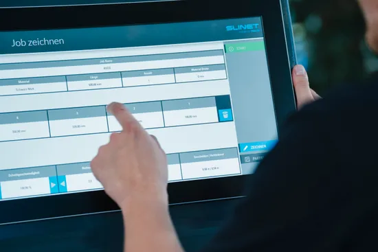 Mitarbeiter bedient die Slinet S-Touch Maschinensoftware über einen Touchscreen mit tabellarischer Übersicht der Maschinen- und Auftragsdaten.