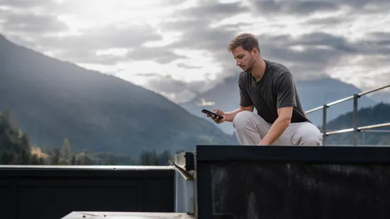 Mitarbeiter nutzt die Variobend V-Mobile App auf einem Smartphone zur mobilen Profilplanung im Außenbereich vor einer Bergkulisse.