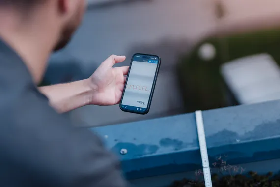 Mitarbeiter nutzt die Variobend V-Mobile App auf einem Smartphone auf einer Baustelle am Dach