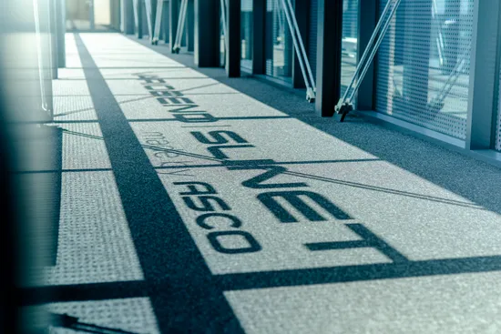 Detailaufnahme des ASCO Group Schriftzugs auf einer metallischen Oberfläche mit industriellem Hintergrund.